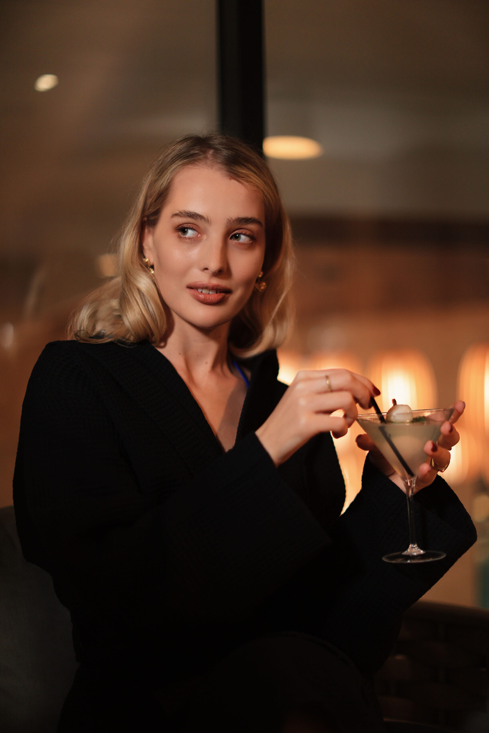 A woman holding a martini glass in a cozy, dimly lit setting.