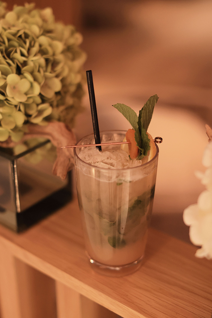 A refreshing cocktail garnished with mint on a wooden table, next to a hydrangea flower arrangement.