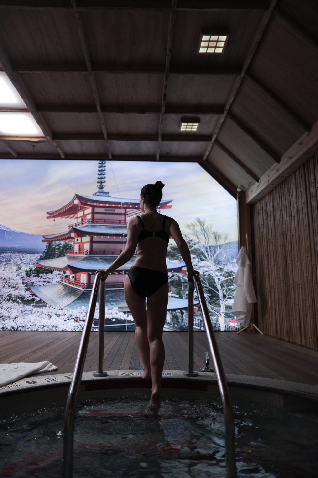 Guest stepping into an onsen pool at World Spa, Brooklyn, beneath the pagoda mural