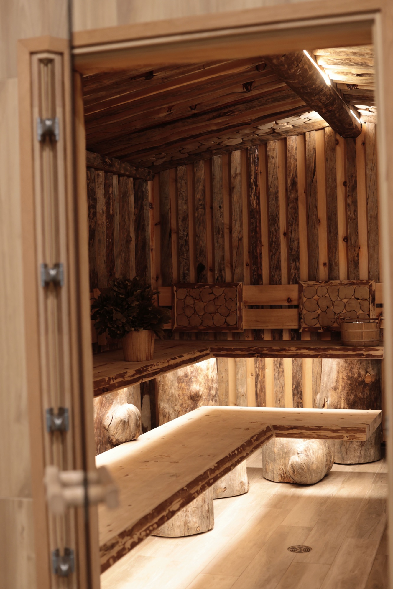 Rustic private banya inside a World Spa lodge, with venik bundles and log benches